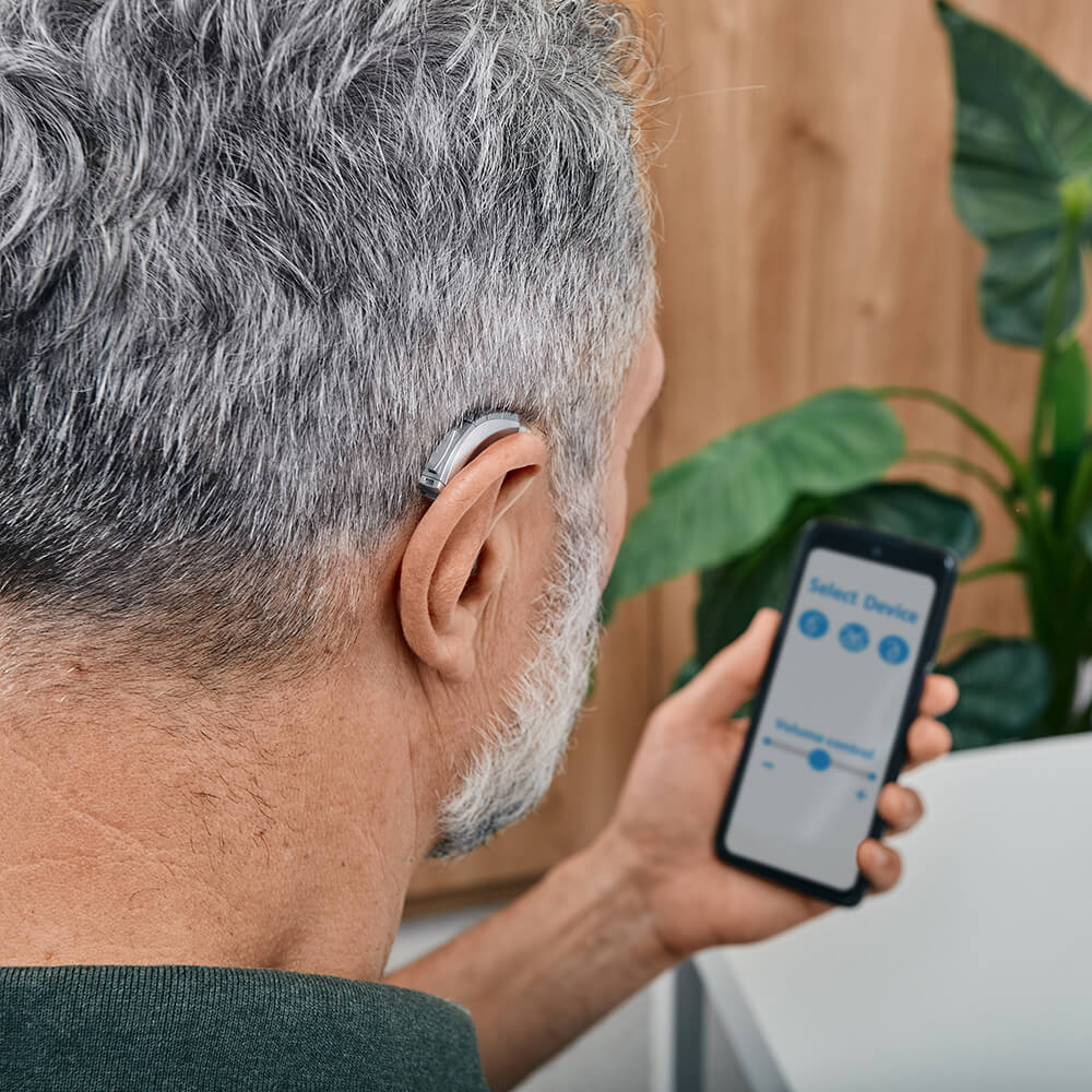 Hearing Impaired Mature Man Wearing Hearing Aid and Adjusting Settings in Smartphone